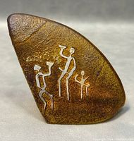 Front view of the amber-colored glass paperweight showing three primitive human figures in white.