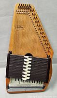 Full front view of a wooden Oscar Schmidt autoharp with chord bars and strings.