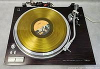 Full top-down view of turntable with gold vinyl record on platter and cables coiled at rear