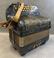 Side angled view showing black pearlescent marbled casing, gold-tone grille with HOHNER branding, and cream-colored buttons.