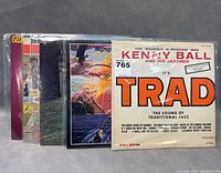 Photo showing 5 vintage vinyl LP records stacked side by side with visible album covers including Kenny Ball's It's Trad and a psychedelic art LP cover.