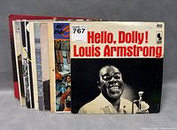 Stack of vintage vinyl LP records showing the front cover of 'Hello, Dolly!' by Louis Armstrong in good condition, with several other LPs partially visible behind.