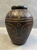 Front view showing carved tribal face with geometric triangle design on top band.