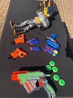 Full view of Batman action figure lying down with four Nerf toy guns and foam darts and discs arranged on black surface.