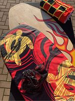 Wooden skim board, boogie board, and rolled checkerboard beach towel with flame designs visible