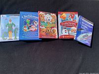 Five DVD cases laid out on a dark surface showing covers of Elf, Christmas Television Favorites, Santa Buddies, The Original Christmas Classics, and DVD Cleaning Disc.