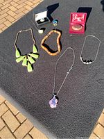 Costume jewelry including necklaces, rings, and a pin displayed on dark fabric outdoors.