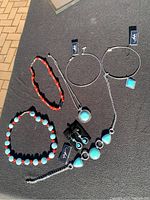 Photo showing all 6 necklaces and 1 pair of earrings arranged on black cloth outdoors, displaying turquoise and red bead color variations.