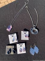 Full lot overview showing two necklaces and five pairs of earrings laid out on black background.