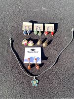 Full view of six pairs of clip-on earrings and one flower pendant necklace arranged on black surface in sunlight.