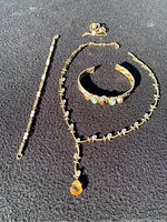 Photo of necklace, two bracelets, and brooch laid out on a dark surface showing the amber and clear stones with gold-tone metal.