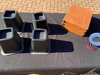 Four black plastic couch risers, square base, on a black cloth surface outdoors alongside a wooden box containing a microscope.