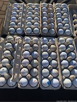 Photo showing multiple cardboard trays filled with used golf balls, mainly Pinnacle and Ultra brands, arranged in rows with visible wear including dirt and scuff marks.