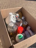 Photo showing box filled with various cleaning and pest control liquids, some in clear bottles, some in spray bottles and jugs.