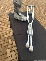 Crutches standing next to left leg aircast boot on black surface outdoors.