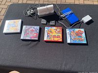 Overview on black mat showing two consoles on stand, six game cases/cartridges, charger and case