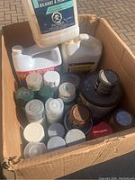 Box filled with assorted paint, stain, and cleaning containers, showing tops and lids.
