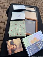 Photo showing six picture frames including a large black frame, a wooden frame, a decorative floral frame with dragonflies, and three smaller frames, plus two photo albums with floral covers.