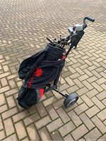 Side view of golf bag mounted on a black and red push cart on pavement, showing clubs inside the bag.