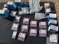 Overview of all boxes and plastic bags containing various wood screws on a dark surface outdoors.