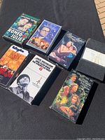 Six VHS tapes on a black surface: Romeo and Juliet, The Reluctant Debutante, Dead Poets Society, One Flew Over the Cuckoo's Nest, A Midsummer Night's Dream, and a plain labeled tape Lord of the Flies.
