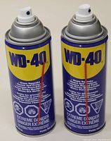 Front view of two WD-40 cans with visible branding, hazard symbols and usage claims.
