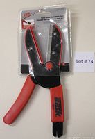 Front view of Task Utility Cutter in original blister packaging showing red handles and black cutting blade.