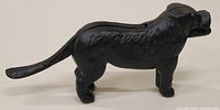 Side view of a cast iron black dog figurine with textured fur details, standing on four legs, tail extended straight out.