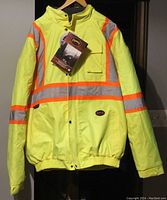 Front view of chartreuse conspicuity coat featuring reflective bands and front pockets with tags attached indicating original condition.
