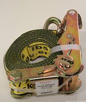 Yellow ratchet tie down strap rolled and secured by white plastic tie, showing ratchet mechanism.