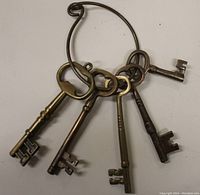 Five vintage brass skeleton keys of varying design, attached to a large brass key ring, viewed from an angle showing key details.