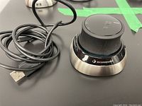 Side angle showing Space Mouse B with USB charging cable coiled next to it on black surface.