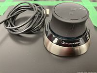 3DConnexion Space Mouse showing the device from the top angle along with a USB charging cable.