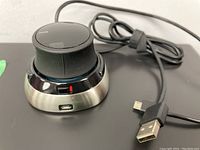 Image showing the 3DConnexion SpaceMouse from the side with USB charging port and cable attached for scale and details.