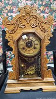 Front view of ornate wooden clock with carved detail and closed glass door showing clock face and pendulum.
