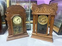 Photo showing both antique wooden mantel clocks side by side on a white surface with purple background.
