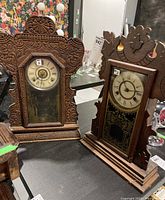 Both antique wood frame clocks together on a table showing front details and size relation.
