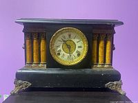 Front view of the antique black mantel clock with gold-tone trim and decorative columns.