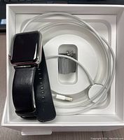 Apple Watch Series 3 with 42mm stainless steel case in original box alongside black leather band, stainless steel Milanese loop band, and white magnetic charging cable coiled in box.