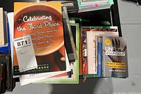 Top view of a stack with 'Celebrating the Third Place' book on top and various others below including hardcover and paperback books.