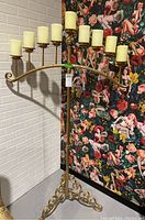 Full view of the metal candelabra showing nine candle holders with ivory-colored candles and the curved horizontal support bar attached to a vertical rod and three-legged base.