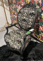 Front angle view of the ornate arm chair with black carved wood frame and black and white floral patterned upholstery.