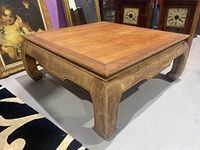 Front angled view of the wooden coffee table showing the flat top and curved carved legs.