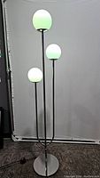 Floor lamp with three lights off-white glowing frosted glass shades at different heights with metal base and stems.