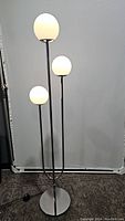 Floor lamp with three frosted glass globes on varied height metal stems with round metal base, all lit in white light.