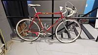 Side view of complete bicycle showing red frame, chrome fork, drop bars, white saddle, whitewall tires