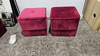 Two velvet pouf ottomans side by side on floor with visible carpet pattern. One ottoman light red/pink and the other dark red/burgundy. No legs attached, wood legs placed nearby.