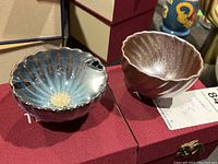 Two small Tenmoku glazed teacups on a red fabric surface, showing their shapes and glazes