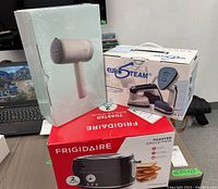 Photo showing the three boxed items: Kexi H2 travel garment steamer, Eurosteam Duet iron and steamer, Frigidaire two slice toaster