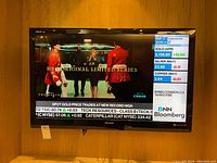 Front view of the Sharp 42-inch TV turned on, displaying a financial news channel with stock prices and weather info.